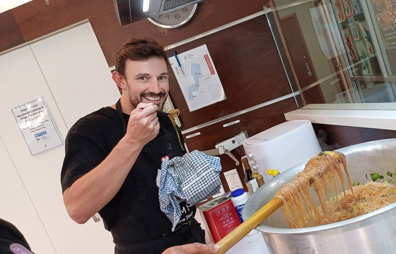 Deadly Ponies employee posing with a large pot of noodles whilst cooking at RMHC Auckland Domain House.